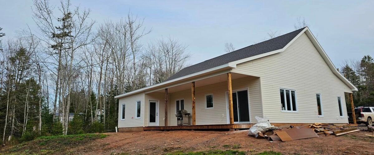 New single-storey home with cream siding and a covered porch on a wooded rural lot