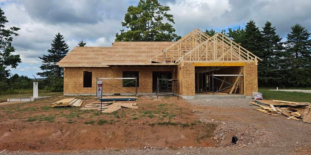 Framed and sheathed single-storey home with roof trusses going up on an open rural lot