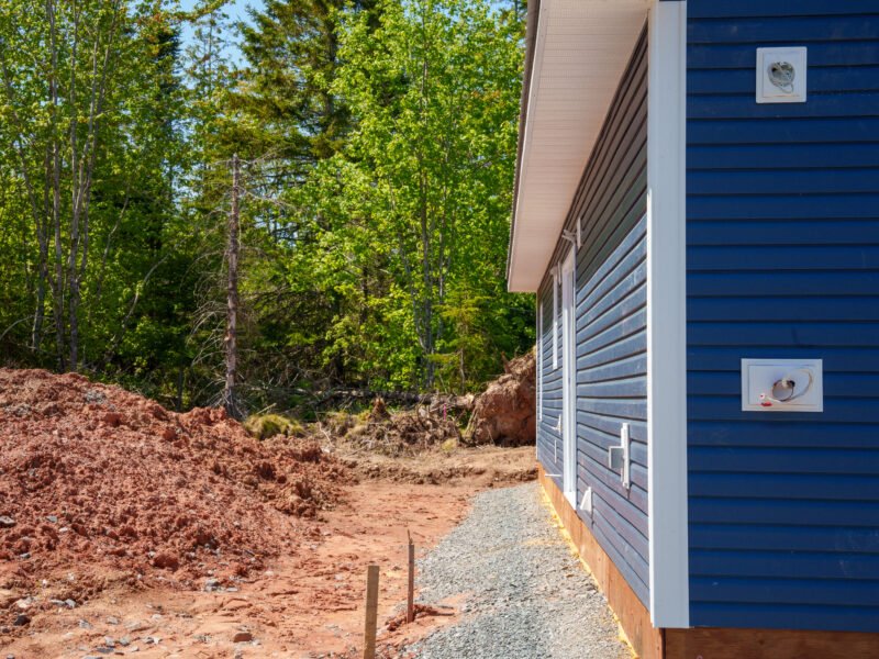 Side wall of a new home with navy horizontal siding beside a cleared lot in East Mountain