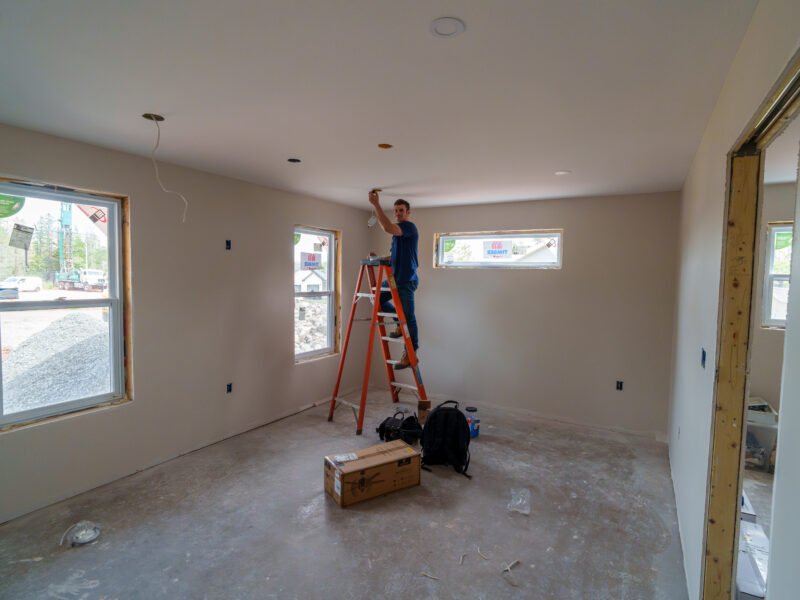Tradesperson installing a ceiling light in a bedroom of a new East Mountain home
